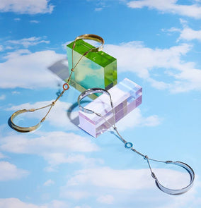 Gold and silver bangle products placed on a bright blue background with white clouds