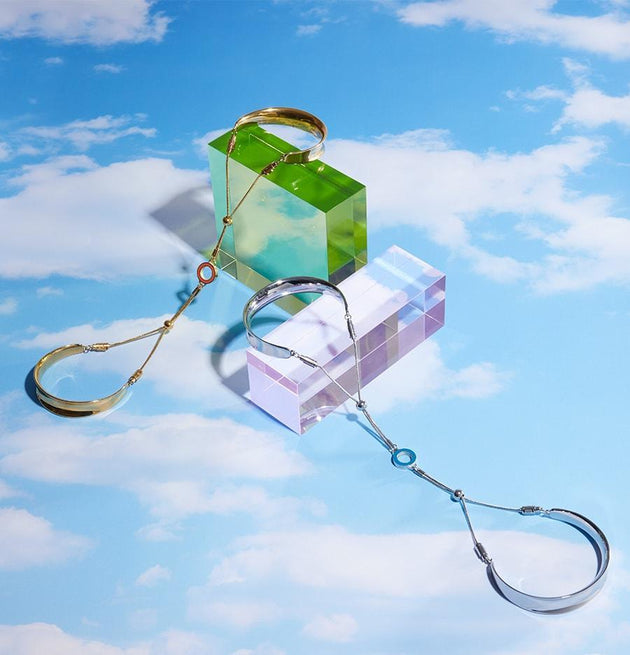 Gold and silver bangle products placed on a bright blue background with white clouds